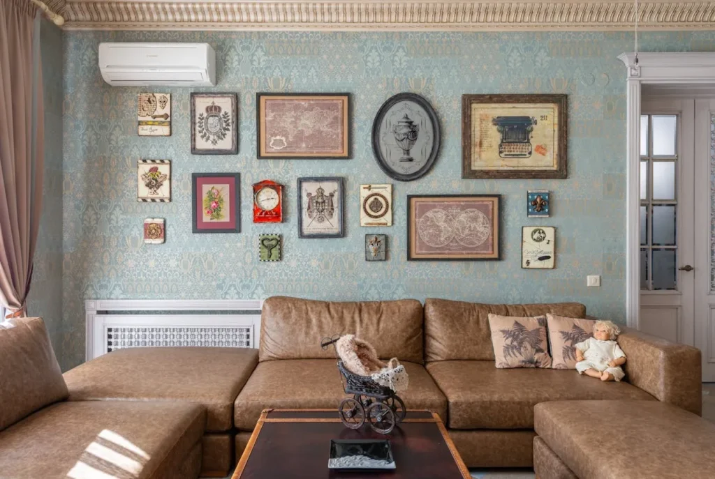 A living room gallery wall with assorted frames holding photos, prints, and a sketch, arranged in a cozy, asymmetrical layout.
